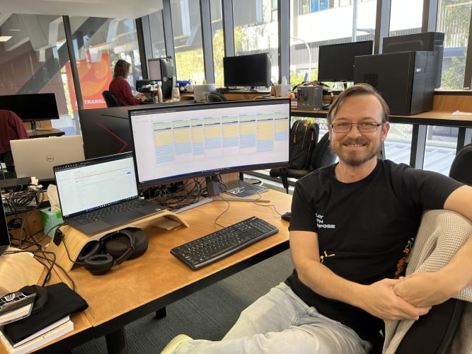 WorkingMouse team member seated at their desk with a large monitor displaying project management tasks, reflecting a productive office environment.